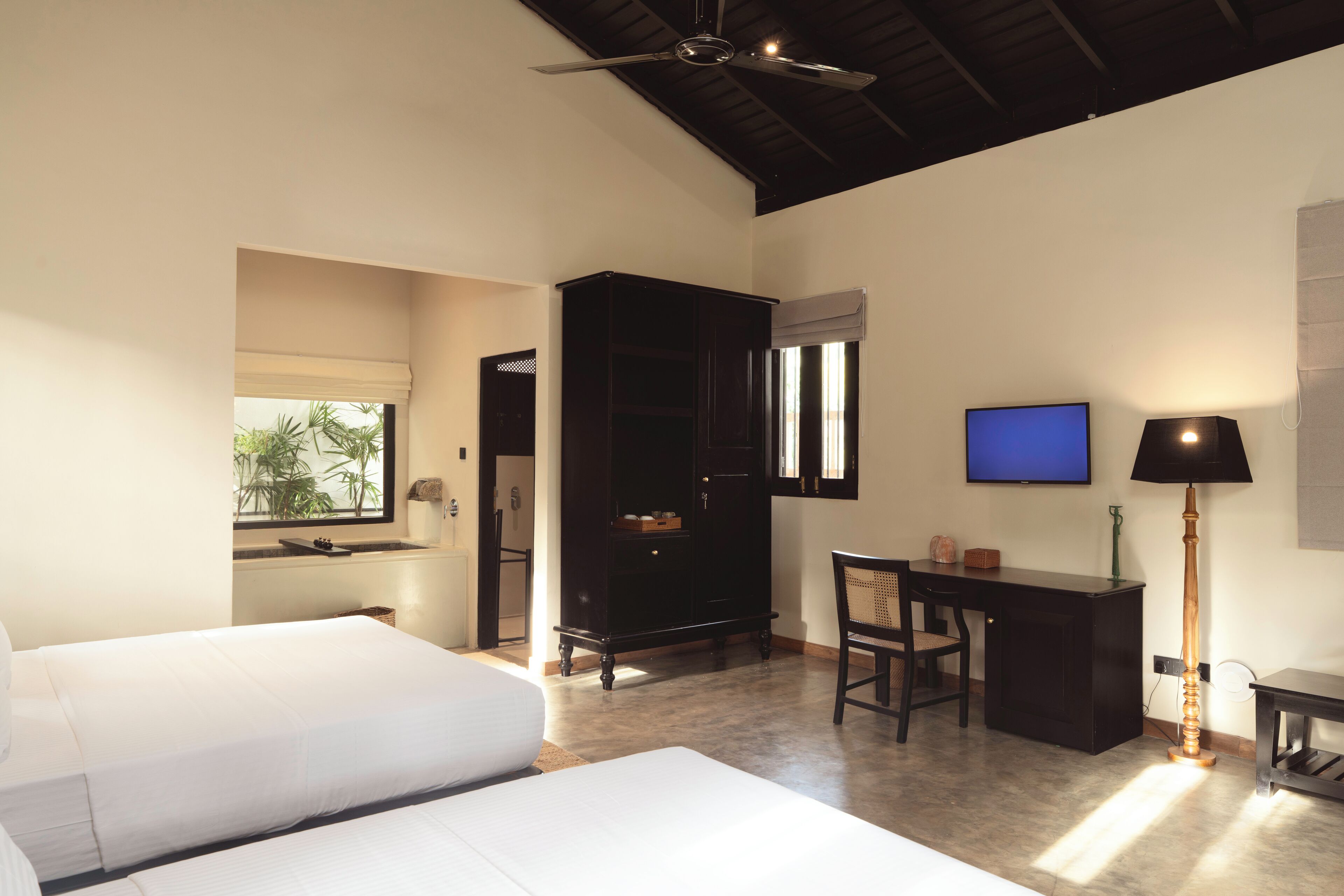 A hotel room with a bed, desk, chair, TV, and a ceiling fan.