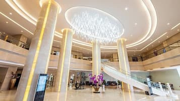 A spacious lobby with a central staircase, multiple floors, and a modern chandelier.