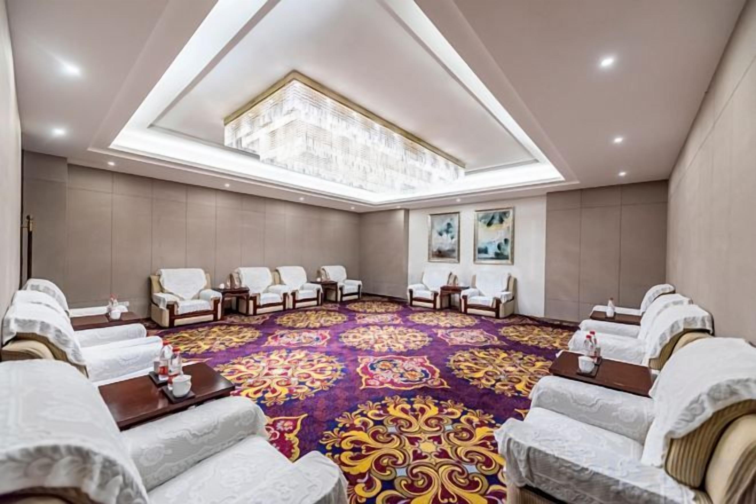 A conference room with a high ceiling, a patterned carpet, and rows of white chairs.