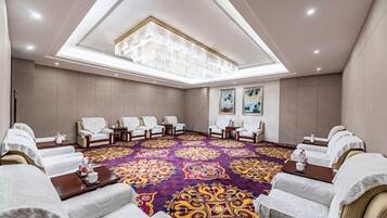 A conference room with a high ceiling, a patterned carpet, and rows of white chairs.