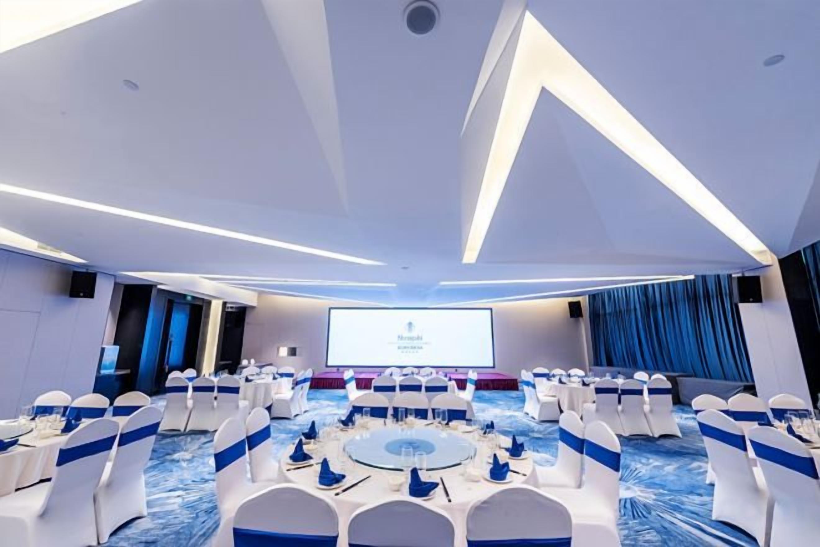 Una sala de conferències amb taules rodones, cadires i una pantalla gran al capdamunt.