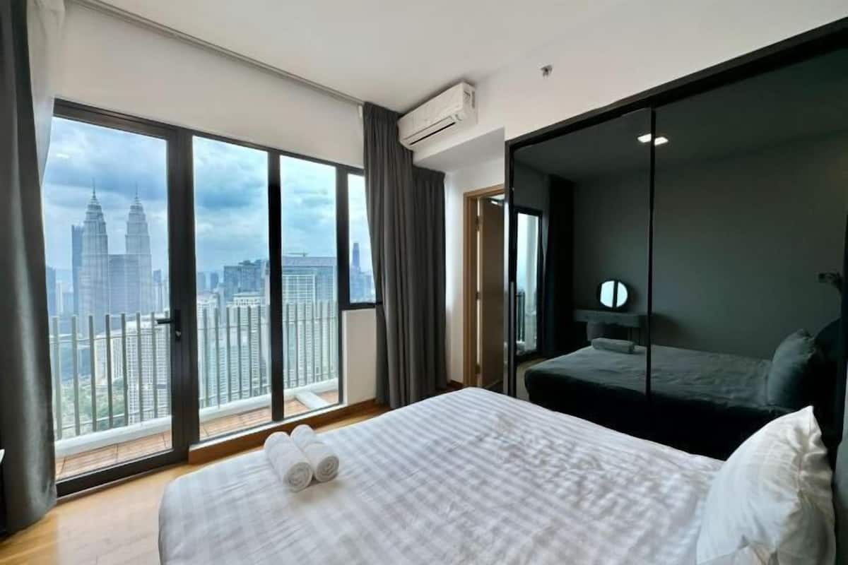 A hotel room with a large bed, a view of the cityscape, and a sliding door closet.