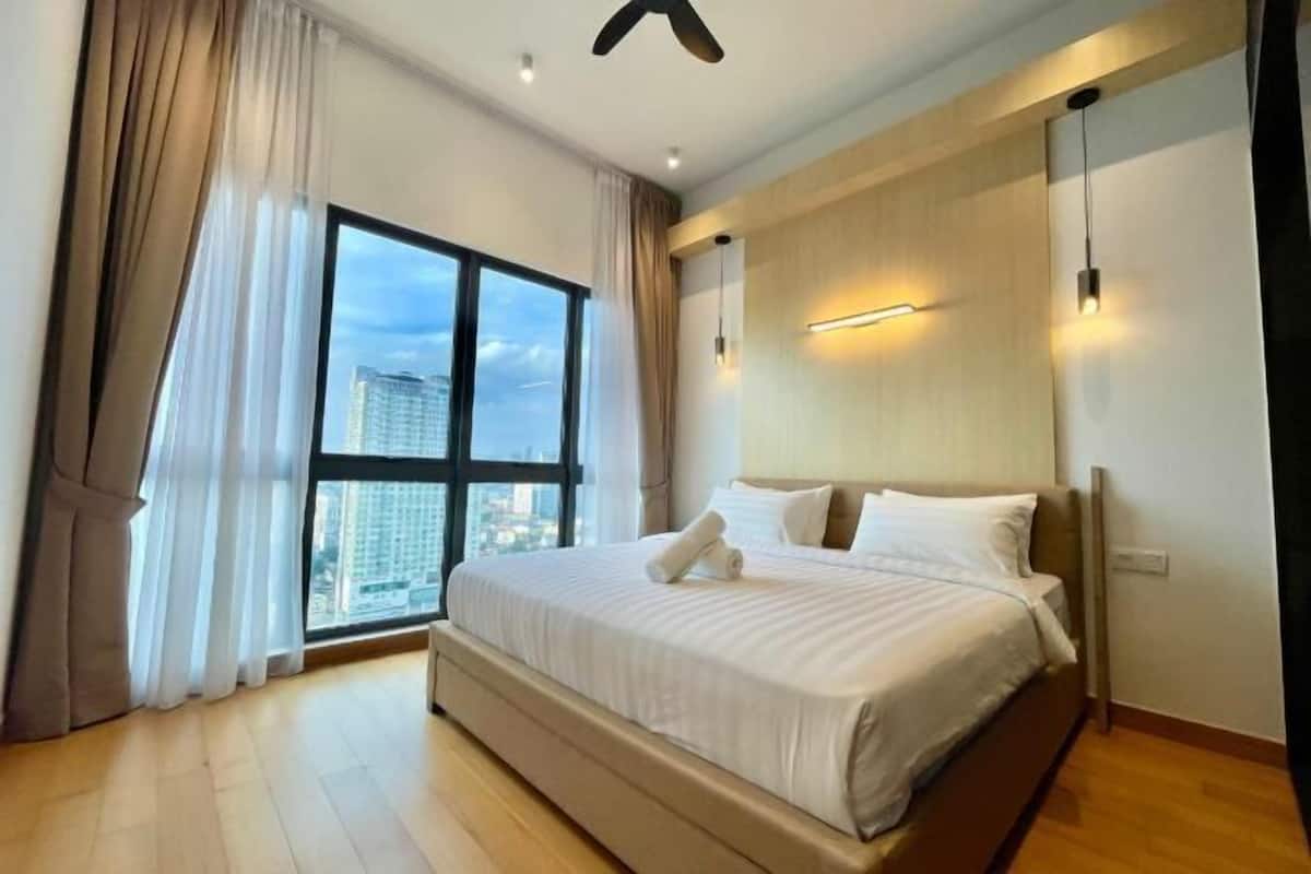 A modern hotel room with a large bed, a view of the city, and a ceiling fan.