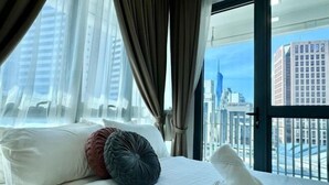 Una habitación de hotel con cama, cortinas y vista a un paisaje urbano.