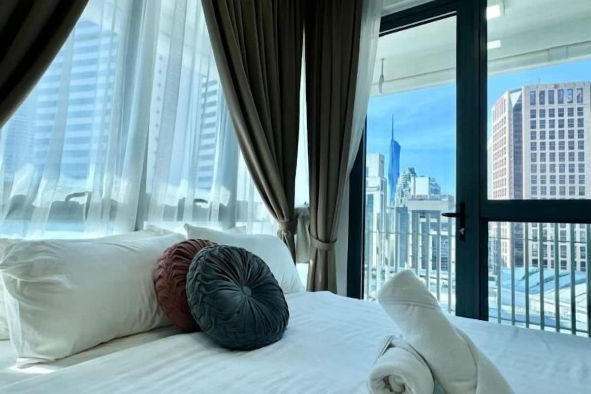 A hotel room with a bed, curtains, and a view of a cityscape.