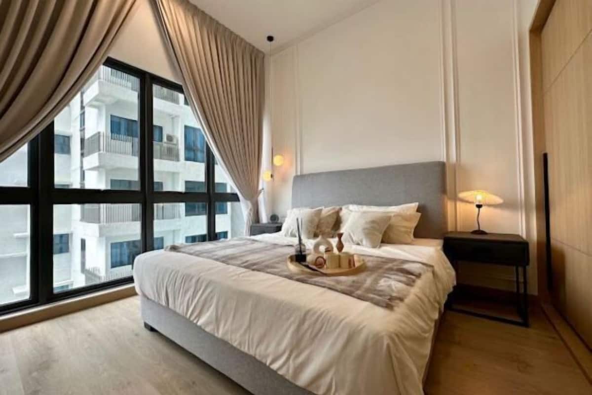 A modern hotel room with a large bed, a nightstand with a lamp, and a view of a building through the window.