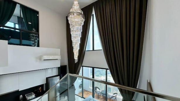 Un interior moderno con una escalera de cristal, una araña y un balcón con mobiliario exterior.