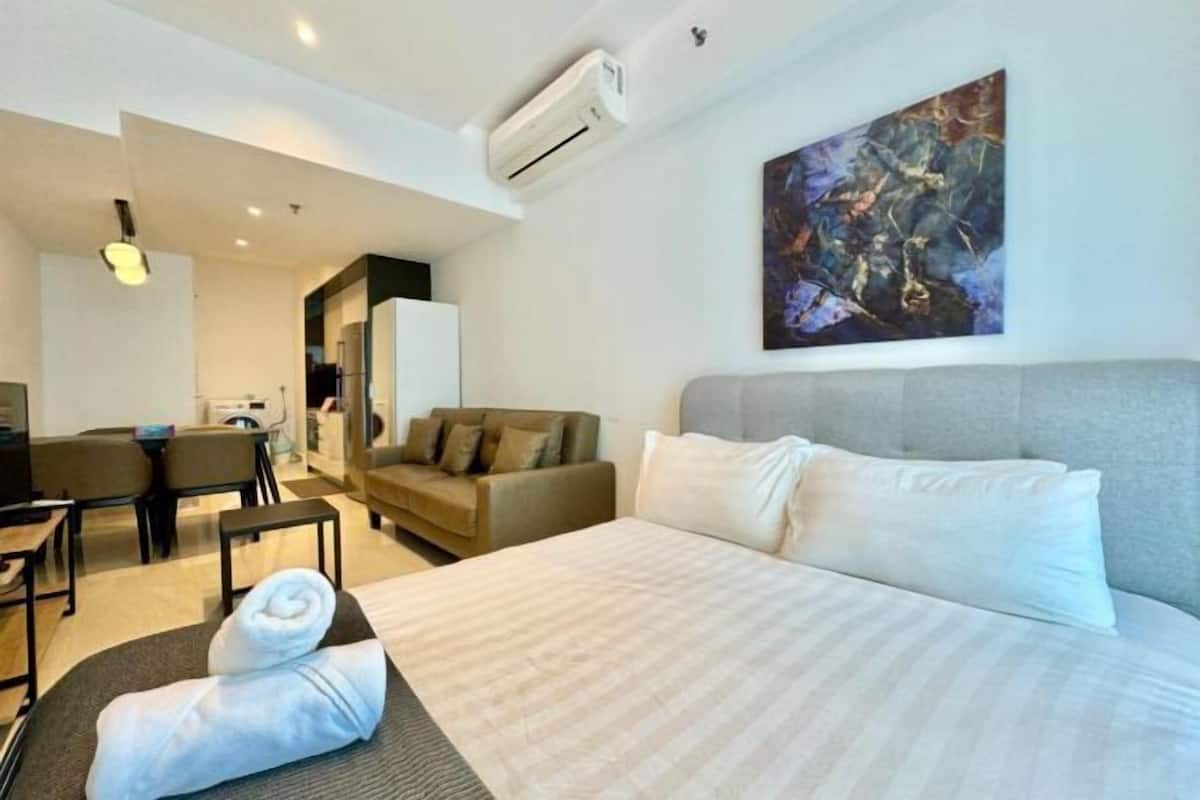 A hotel room with a bed, a sofa, a desk, and an air conditioning unit.