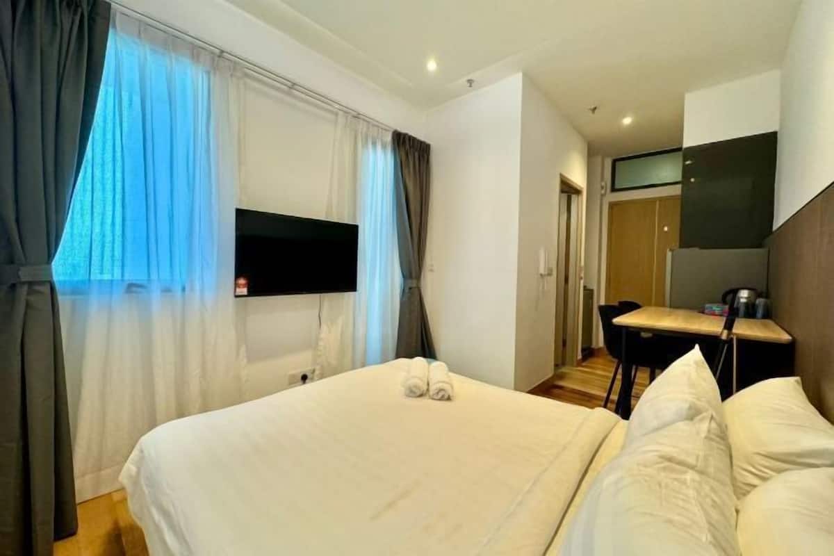 A hotel room with a bed, a desk, a chair, a TV, and a wardrobe.