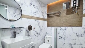 Un baño moderno con salpicadero de mármol, un lavabo blanco, un inodoro y una zona de ducha con panel de madera.
