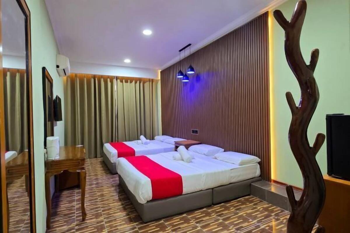 Ein Hotelzimmer mit drei Betten, einem Holztisch, einem Spiegel und einer dekorativen Holzskulptur.
