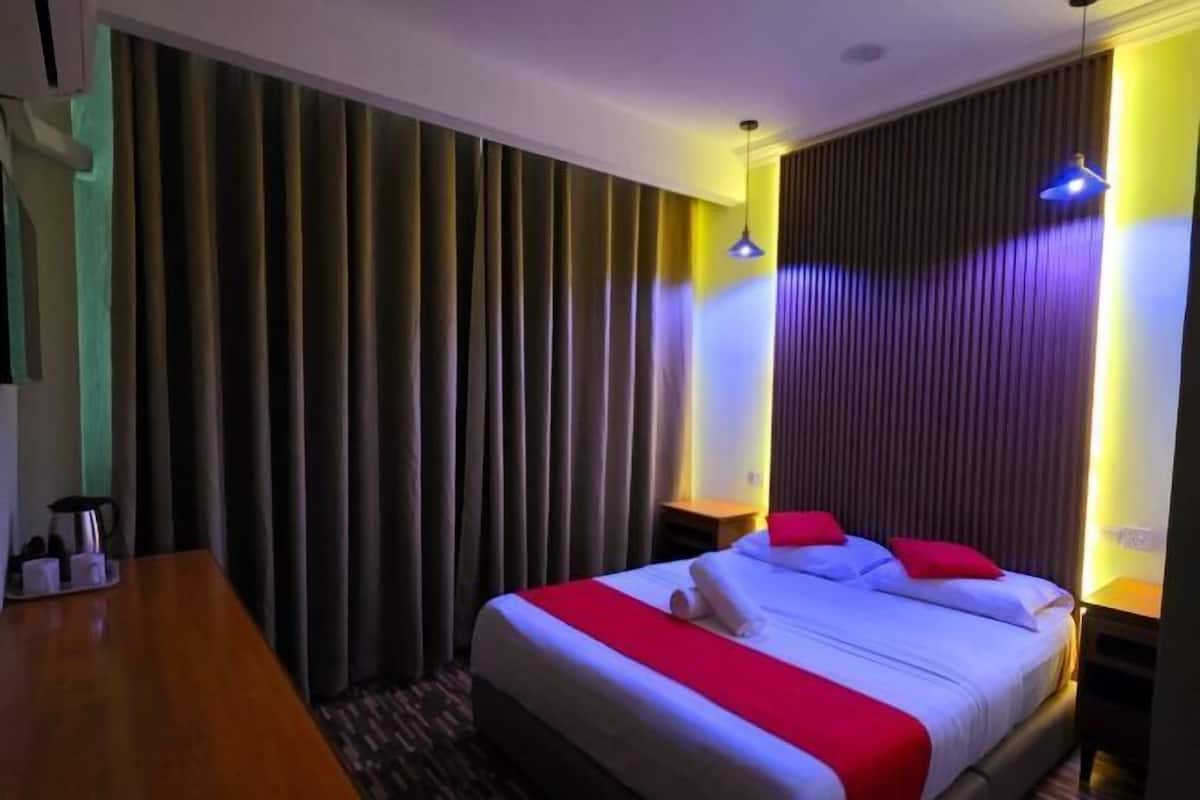 Ein Hotelzimmer mit Bett, einem Holztisch, einem Nachttisch und einer Wand mit vertikalen Jalousien.