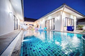 Een modern huis met een zwembad, grote ramen en een overdekt terras.