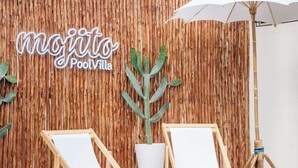 A room with a wooden wall, two white lounge chairs, a potted plant, and a sign that reads "mojito PoolVilla". - Spacious 5-Bed Villa: 7 Mins to Walking Street (Pattaya City)