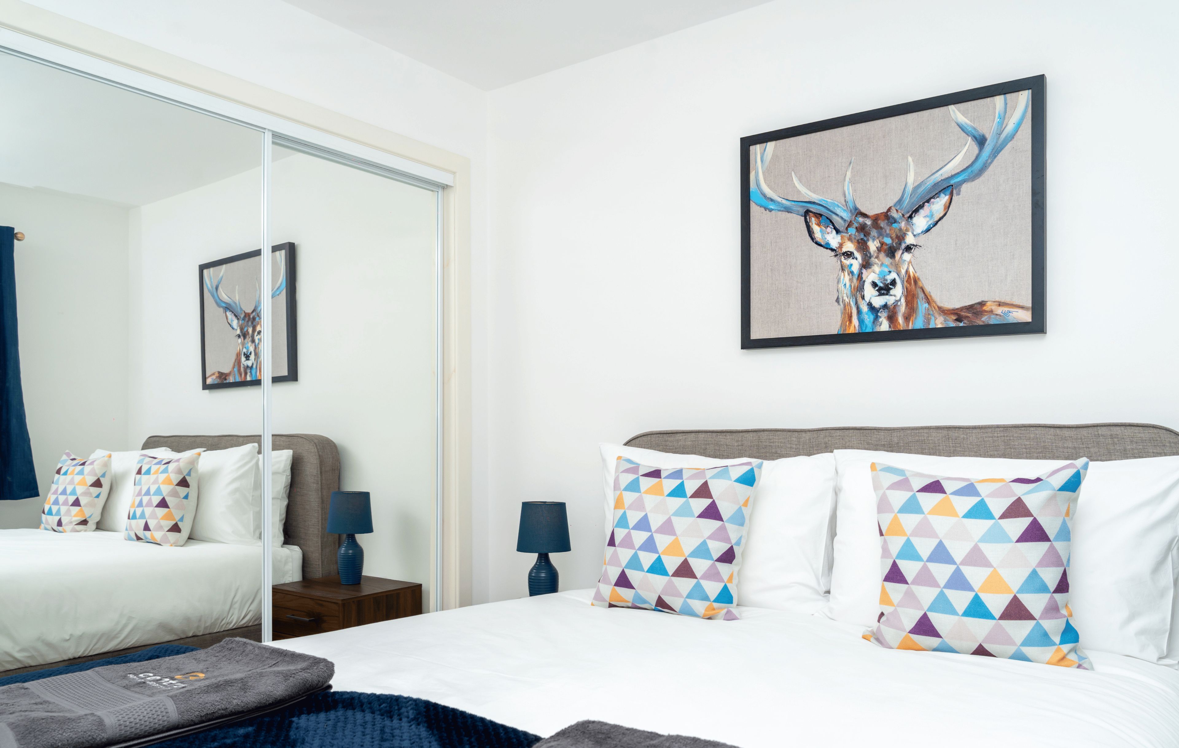 Une chambre d’hôtel moderne avec un grand lit, un miroir et un tableau représentant un cerf.