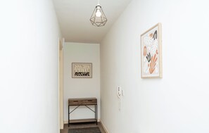 Een gang met een bank, een lamp en twee kunstwerken in lijsten aan de wanden.