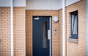 Een moderne entree met een donkerblauwe deur, een beveiligingscodeklavier en een klein raam met gordijn.