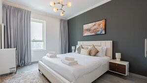 A modern bedroom with a large bed, a bedside table, a nightstand, a window with curtains, and a ceiling light fixture. - Marina Quays Residences - Dubai Marina (Dubai)