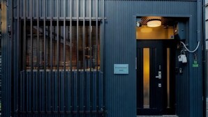 A building entrance with a metal gate, a door with a sign, and a light fixture above the door. - Rakuyado Turuhashi (Osaka)