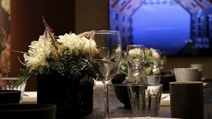 A table set with glasses, a vase with flowers, and a television in the background. - Rakuyado Turuhashi (Osaka)