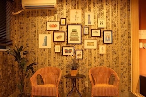 A room with patterned wallpaper, two wicker chairs, a small table, and framed pictures on the wall. - Rakuyado Turuhashi (Osaka)