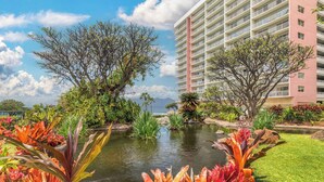 Un hotel con un edificio grande, un pequeño estanque y plantas tropicales.