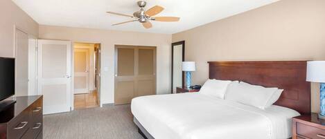 A hotel room with a large bed, a ceiling fan, a TV, and a desk with a lamp.
