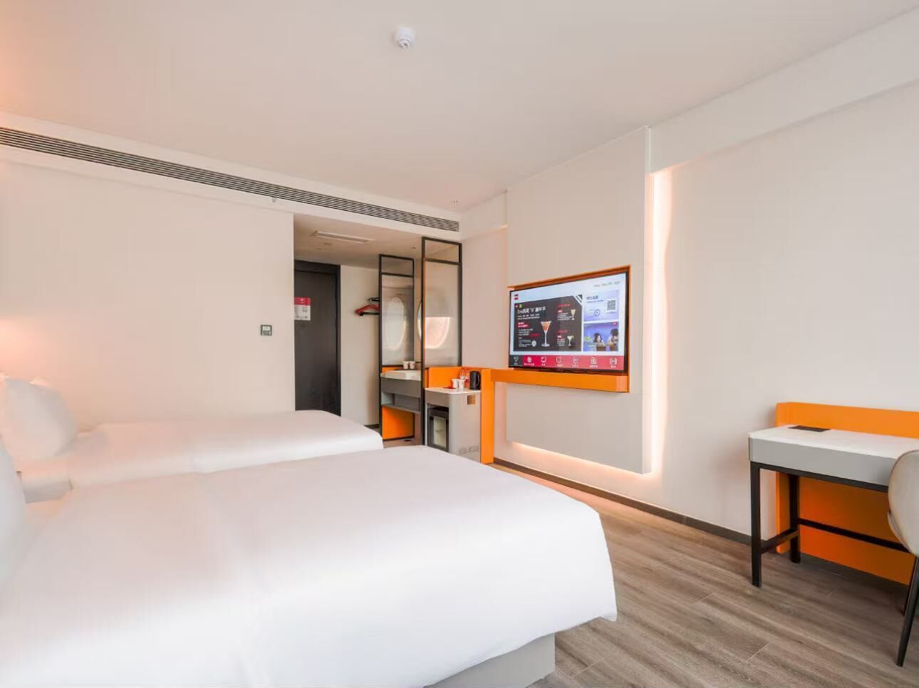 A hotel room with two beds, a desk, a TV, and a mirror.