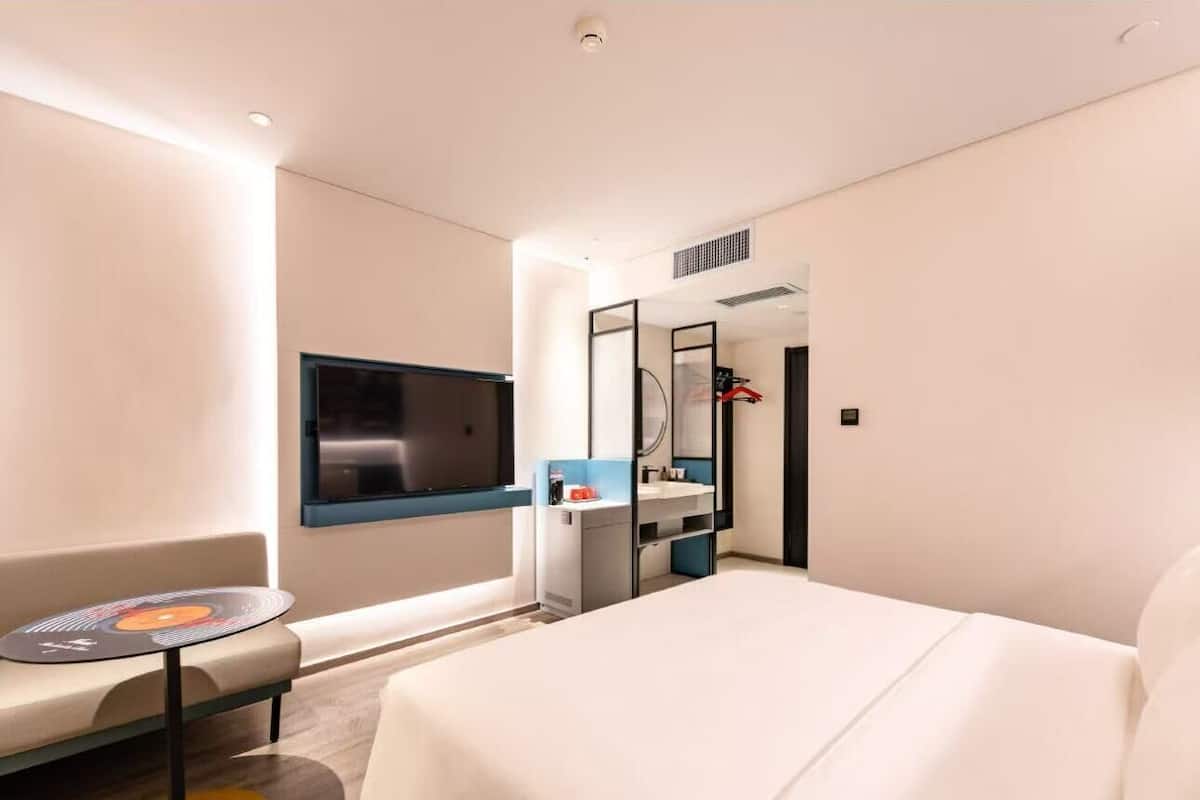 Moderni hotellihuone, jossa on suuri sänky, pieni pöytä ja oleskelualue, televisio ja peili.