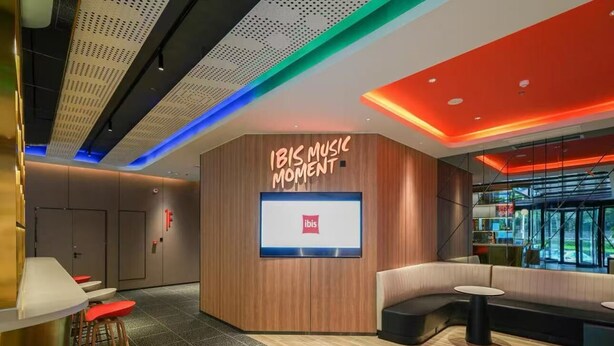 A modern lobby with a curved seating area, a large screen displaying the ibis logo, and a wooden accent wall. - YIBISI (Qingdao)