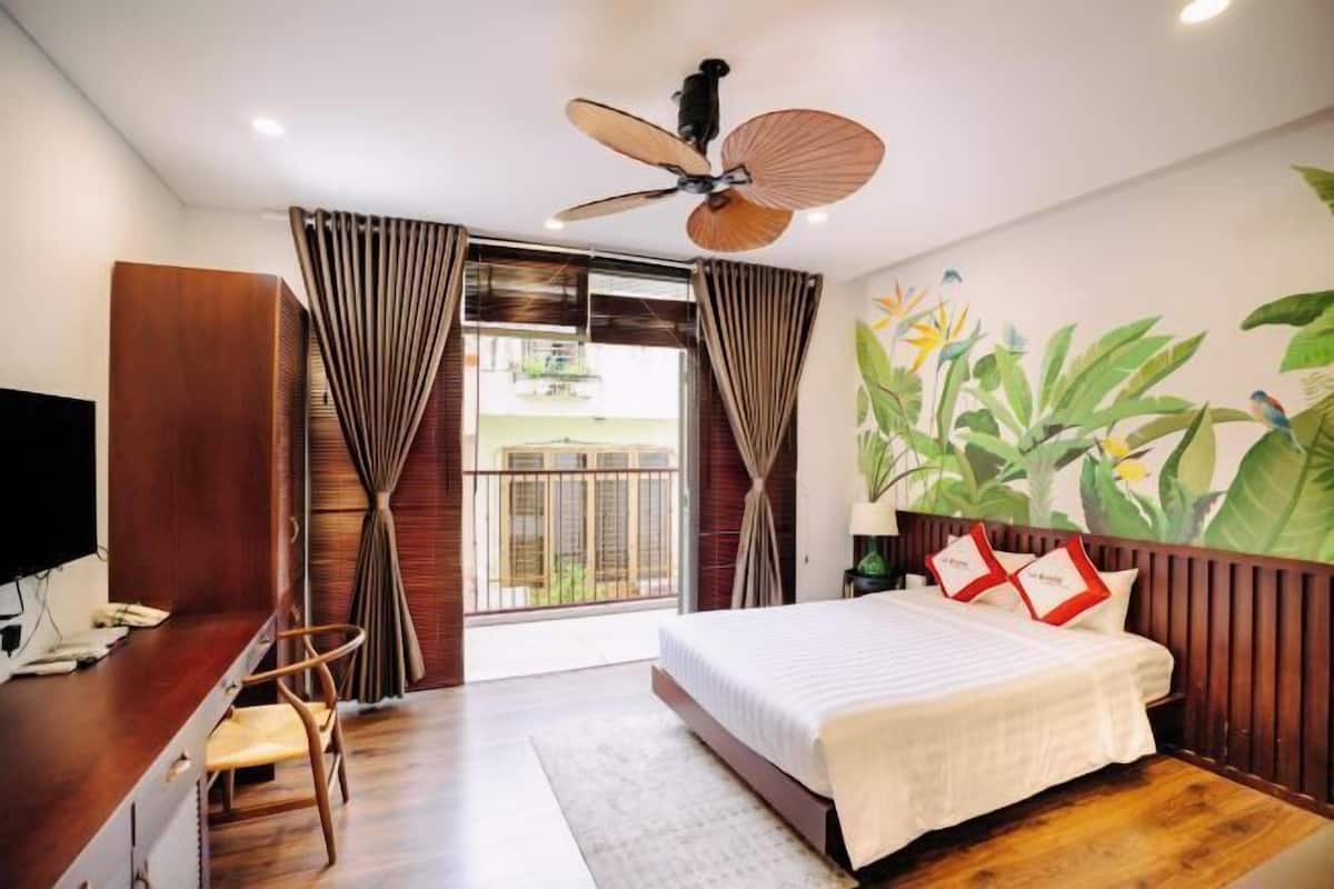 A hotel room with a bed, a desk with a chair, a television, and a ceiling fan.
