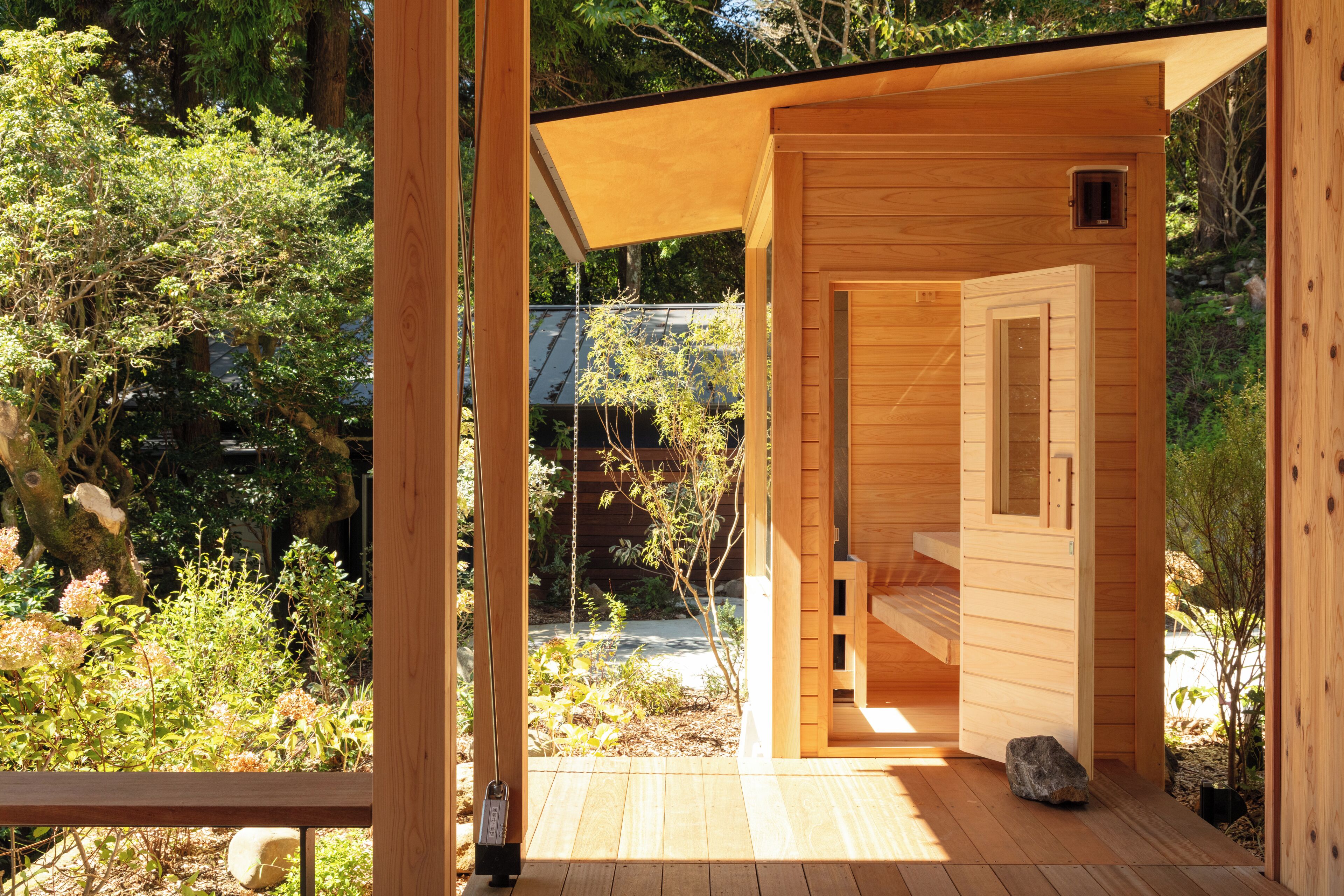 Une structure de sauna en bois dotée d’une porte en verre, entourée de verdure.