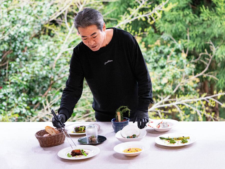 Una persona sirviendo comida en una mesa al aire libre, con diferentes platos y una cesta de pan.