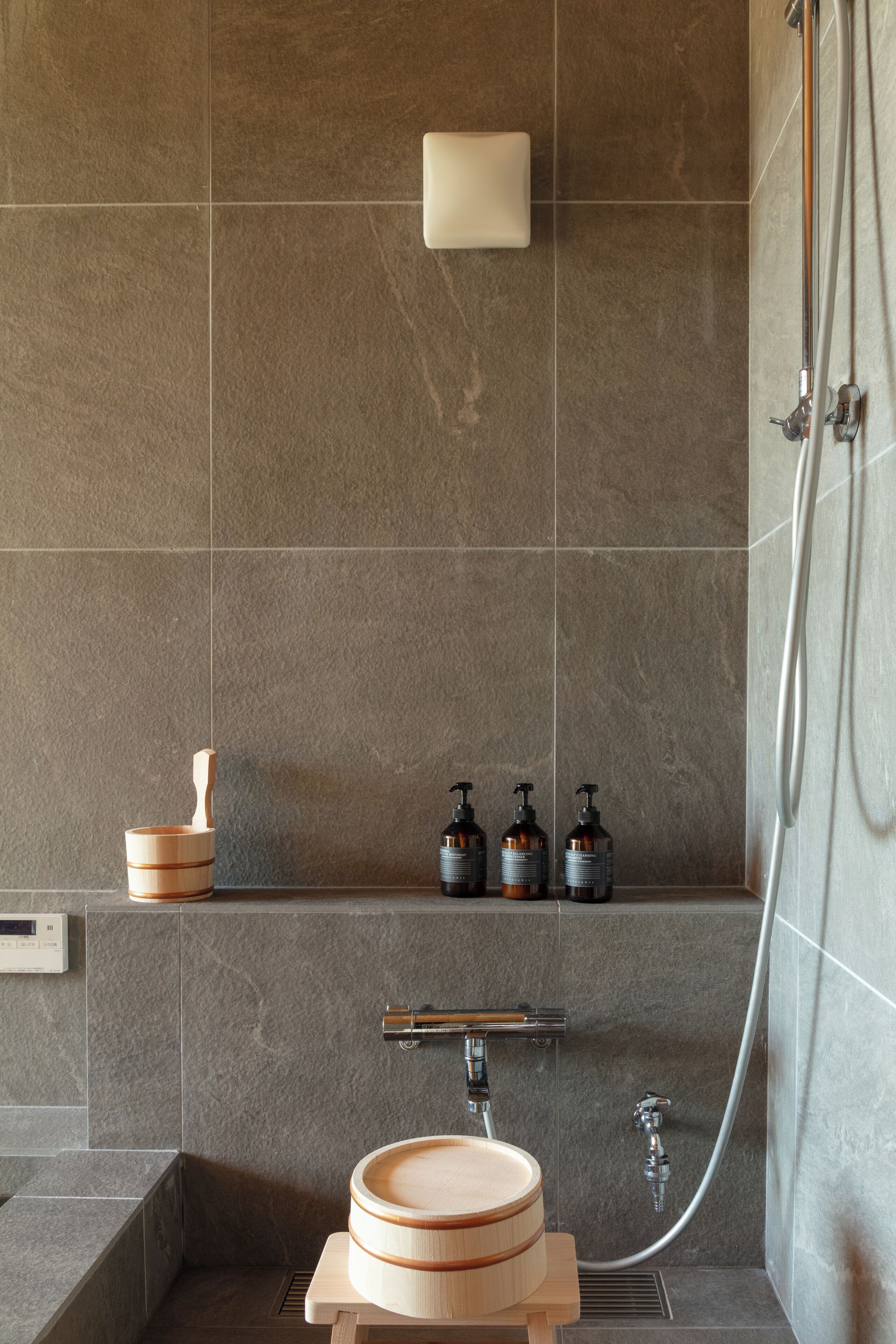 A modern bathroom with a wooden basin, a built-in shelf with toiletries, and a shower area.