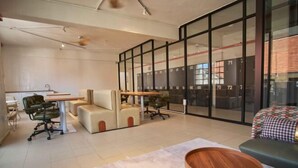 Un espacio de oficina moderno con un amplio separador de vidrio, un sofá, una mesa de madera y un escritorio con una silla.