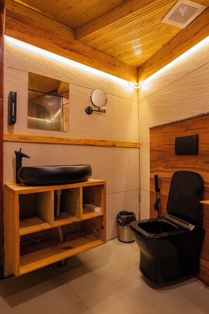 A small, compact bathroom with a wooden vanity, a black sink, a mirror, and a toilet.