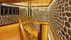 A wooden interior with a stone wall, a wooden staircase, and a window with curtains.