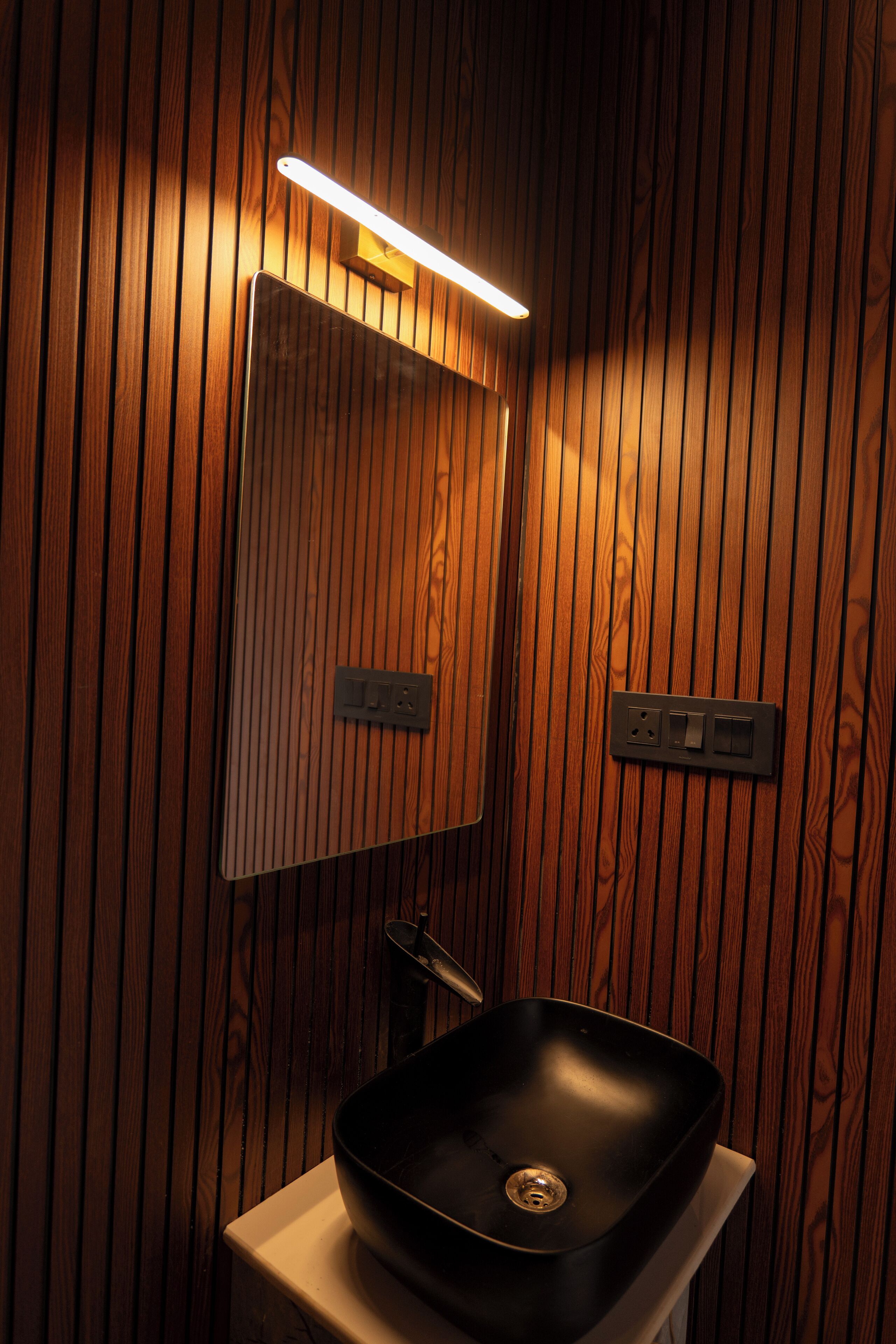 A bathroom with wooden paneling, a black sink, and a mirror with integrated lighting.