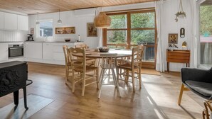 A modern kitchen with white cabinetry, a wooden dining table with chairs, and a large window offering a view of greenery.