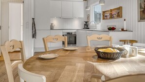 A modern kitchen with white cabinetry, a wooden dining table, and a hanging woven light fixture.