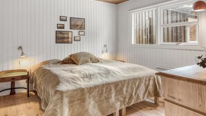 A bedroom with a wooden ceiling, a bed with a beige blanket, a nightstand with a lamp, and a dresser.