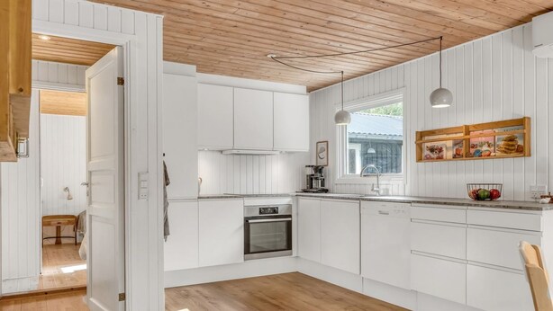 A modern kitchen with white cabinetry, a wooden ceiling, and a window providing natural light.