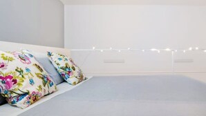 A bedroom with a bed, floral pillows, and string lights. - Suite 18 • Loft Incantevole con Balcone sul Mare di Ortigia (Siracusa)