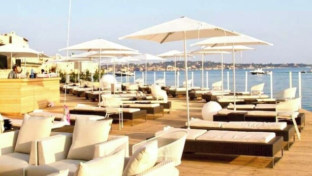 A beachside lounge area with sun loungers and umbrellas, overlooking the sea. - Suite 18 • Loft Incantevole con Balcone sul Mare di Ortigia (Siracusa)