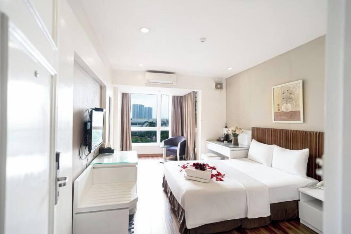 A hotel room with a bed, bedside table, chair, and a view of the city.