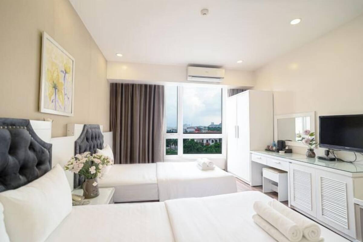 A hotel room with two beds, a desk, a TV, and a large window with curtains.