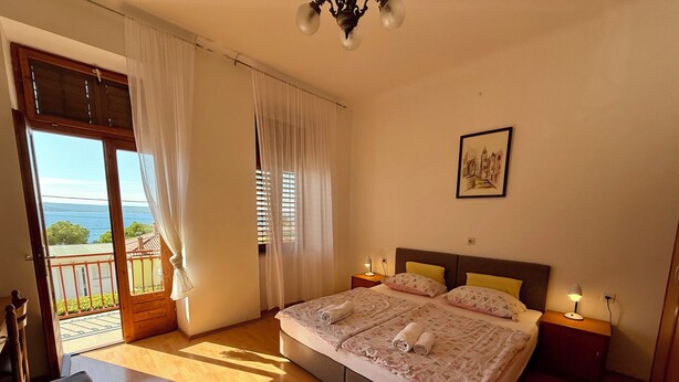 Un dormitorio con una cama grande, dos mesitas de noche, una lámpara de noche, un balcón con vistas al mar y un aplique de techo.