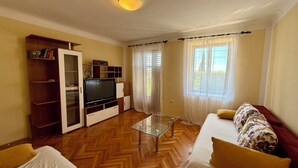 Un salón con televisión, muebles de madera, una mesa de centro de vidrio y un sofá con cojines estampados.