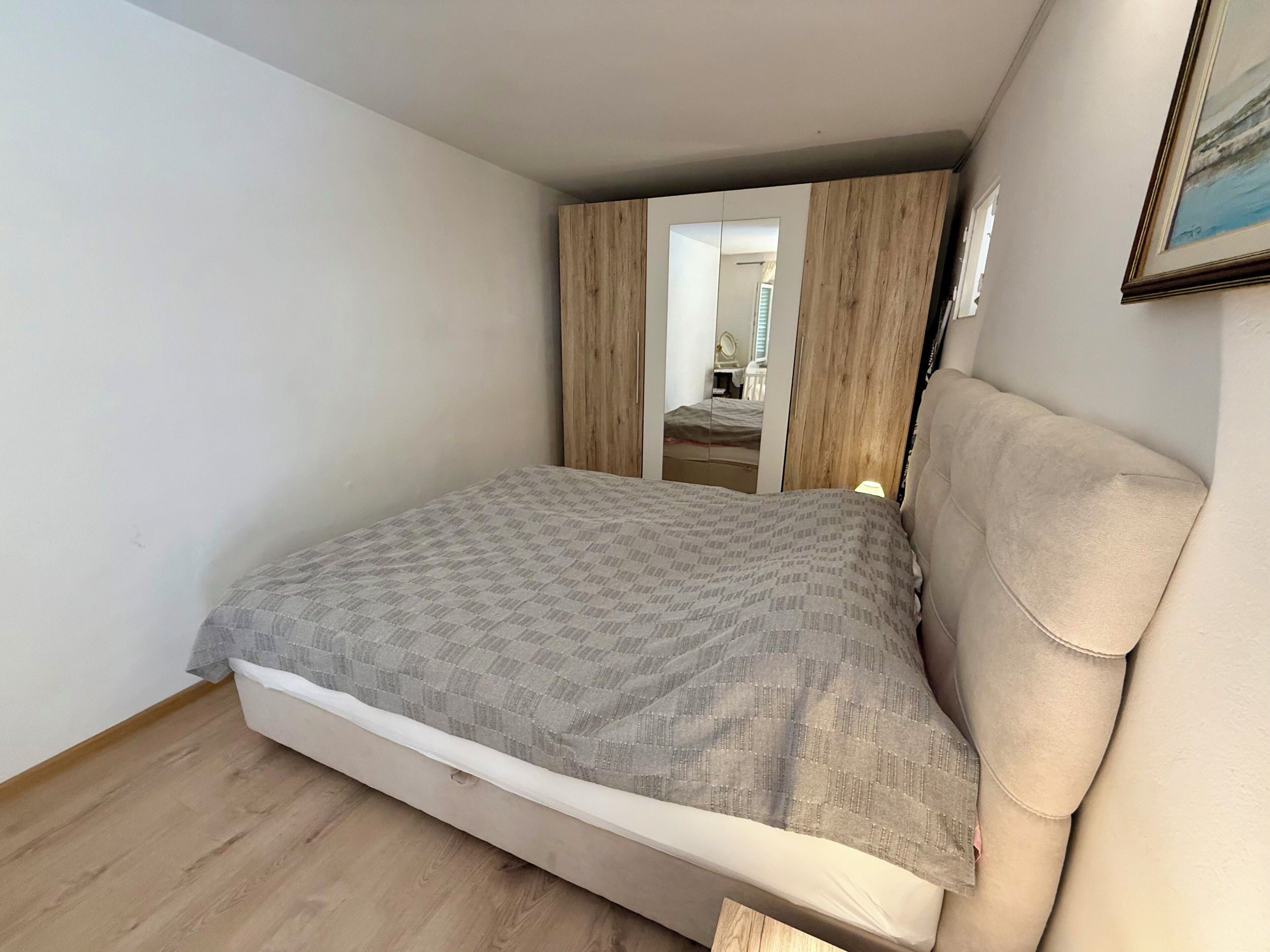 A bedroom with a bed, wooden wardrobe, and a mirror.