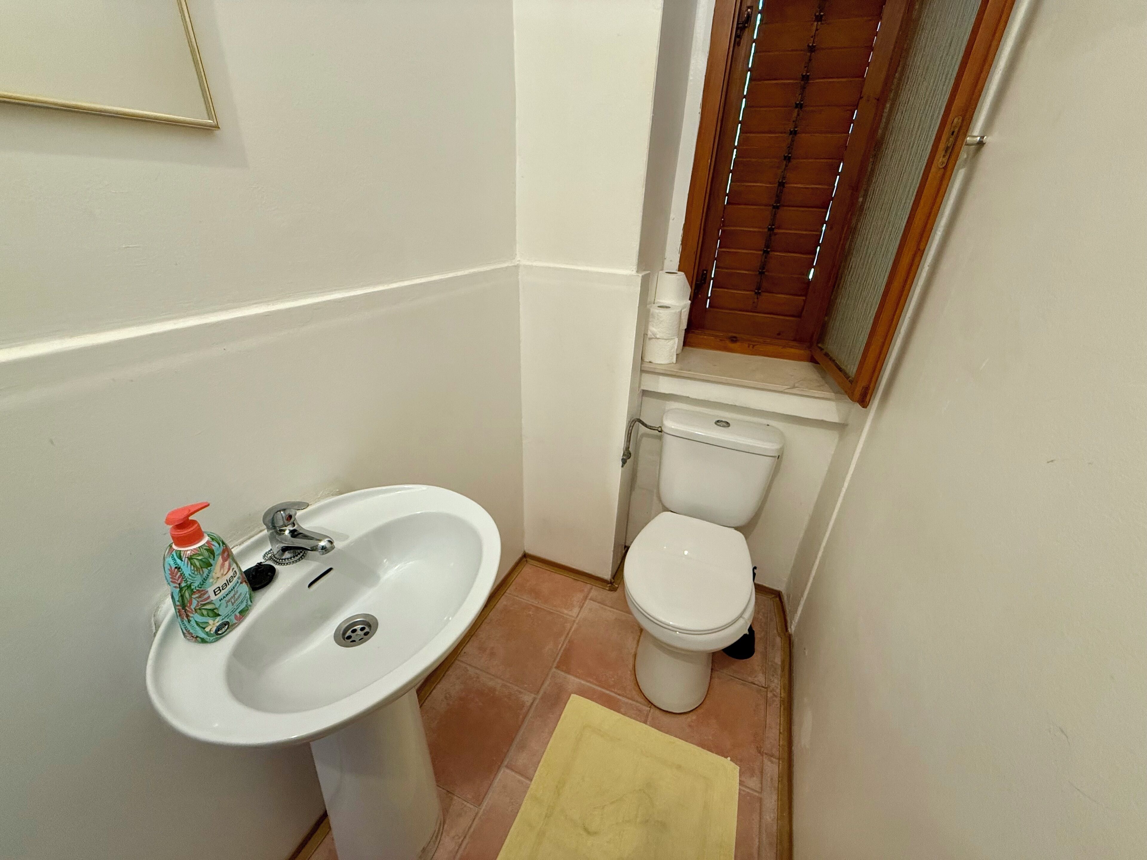 A small bathroom with a white sink, toilet, and a wooden window.